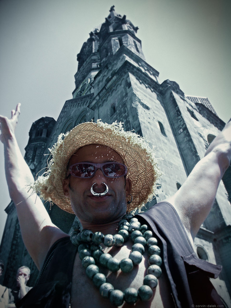 garten-der-lüste-patrice-gedächtnis-kirche-loveparade-berlin-2003-corvin-dalek-com Patrice in a straw hat, sunglasses, and tribal jewelry raising his arms in front of the Kaiser Wilhelm Memorial Church in Berlin.