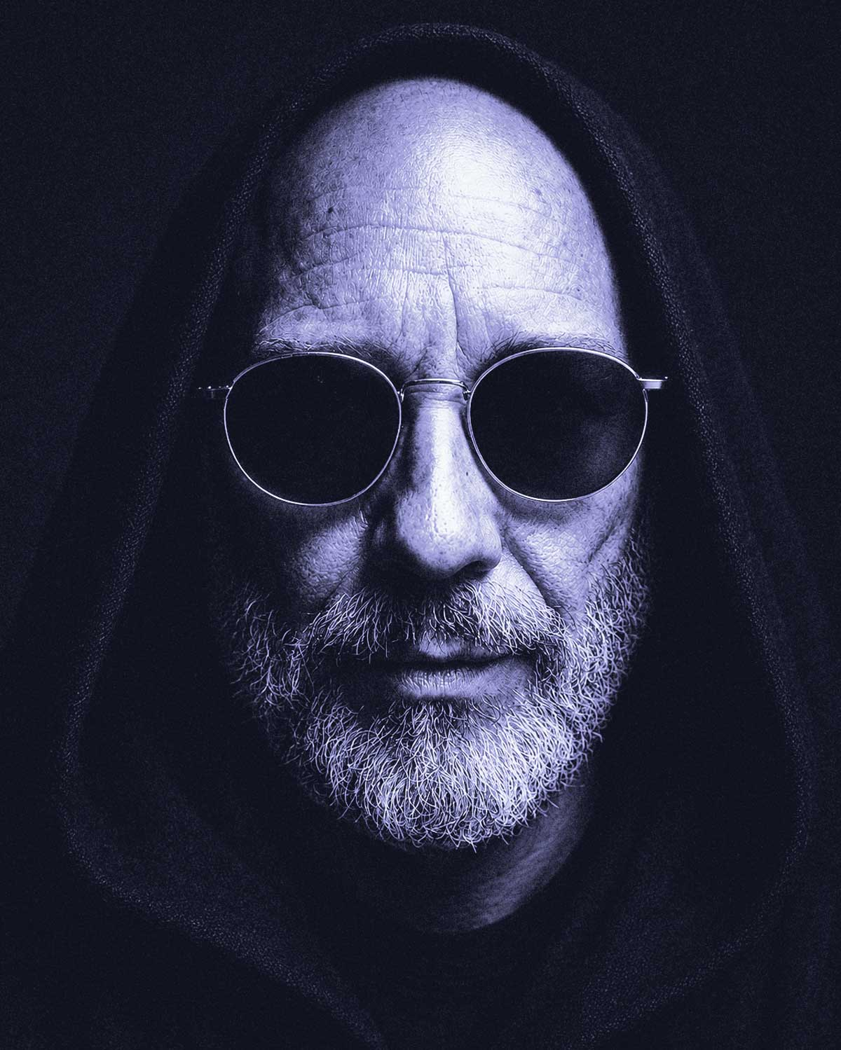 Portrait of Corvin Dalek wearing a hood and round dark glasses.